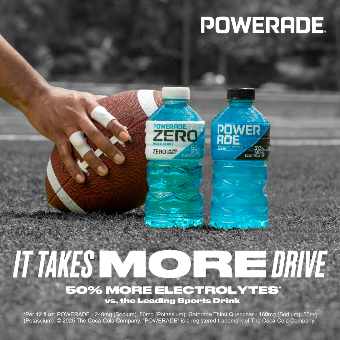 A soccer ball being held by a cleat on a field next to a bottle of Powerade Mountain Berry Blast and a bottle of Bodyarmor